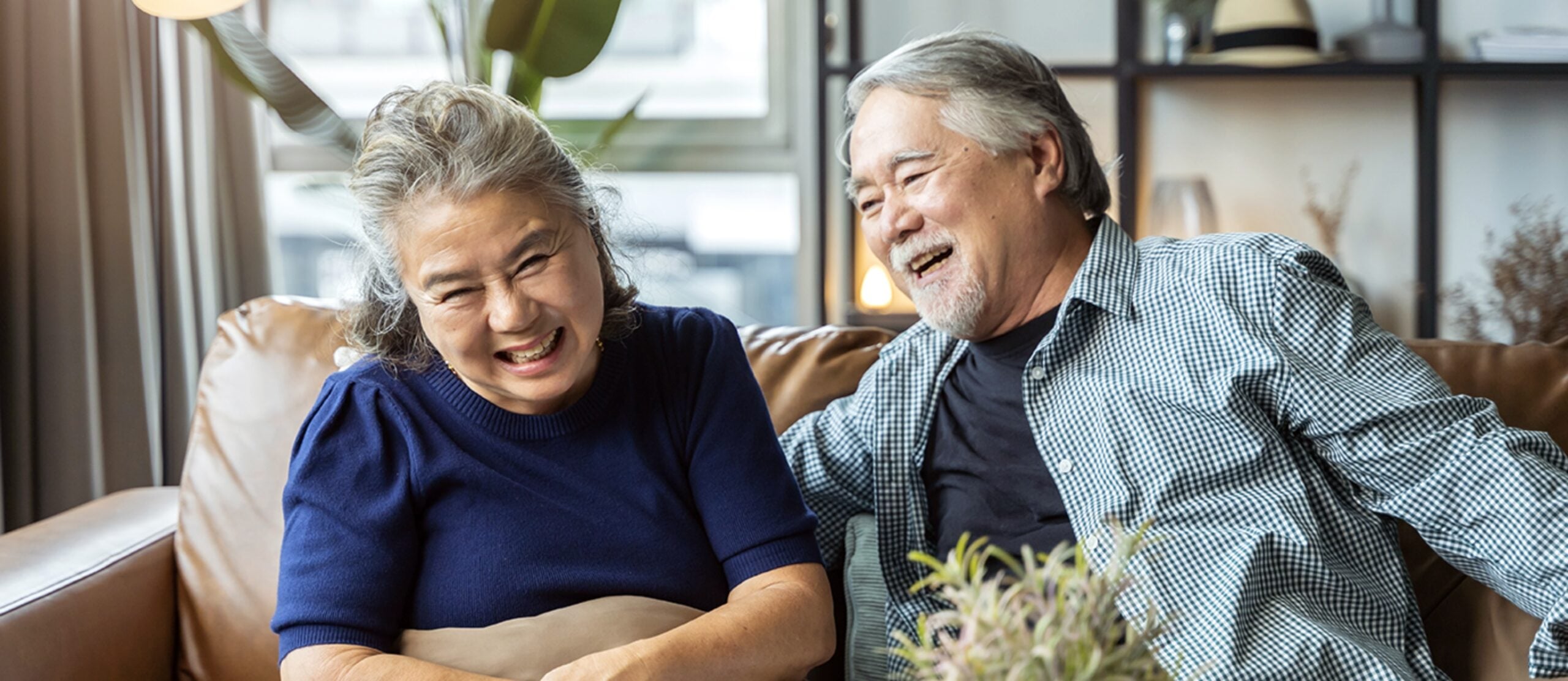 Mature Asian couple laughing together while sitting on a leather couch