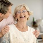 A woman embracing an older woman who is sitting