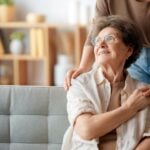 elderly lady sitting on the couch holding a person's hand who is standing behind them